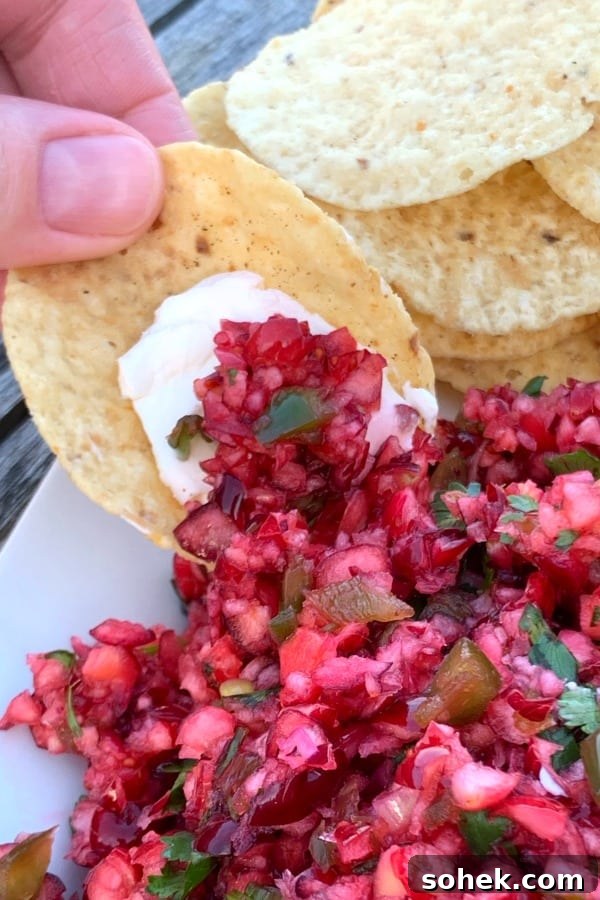 Zesty Cranberry Jalapeño Salsa Recipe for Holiday Parties 2 Thumb holding tortilla chip with cream cheese dipping in cranberry salsa