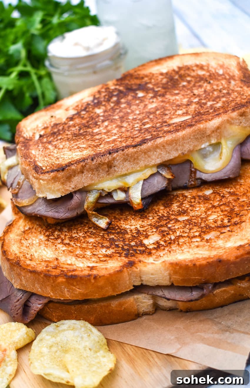 two roast beef grilled cheese sandwiches with smoked gouda stacked together on a wooden cutting board