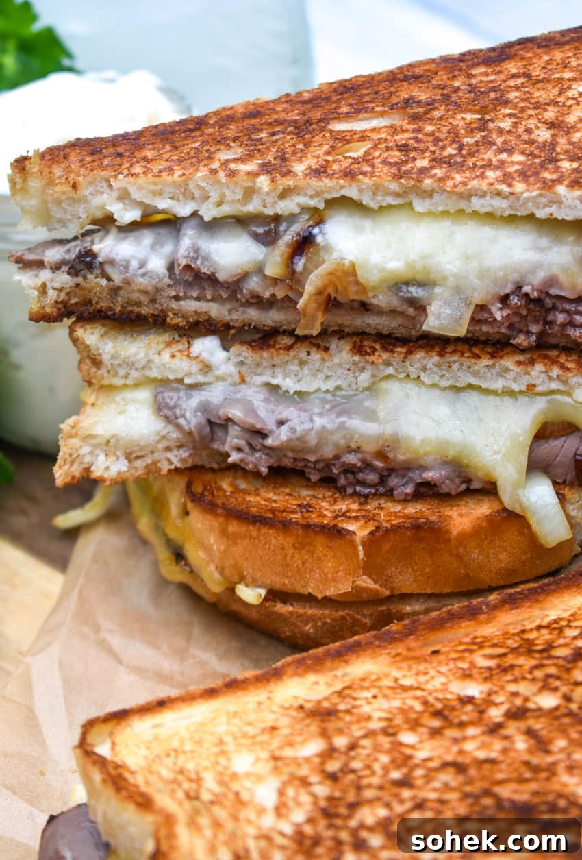 two roast beef grilled cheese sandwiches with smoked gouda stacked together on a wooden cutting board