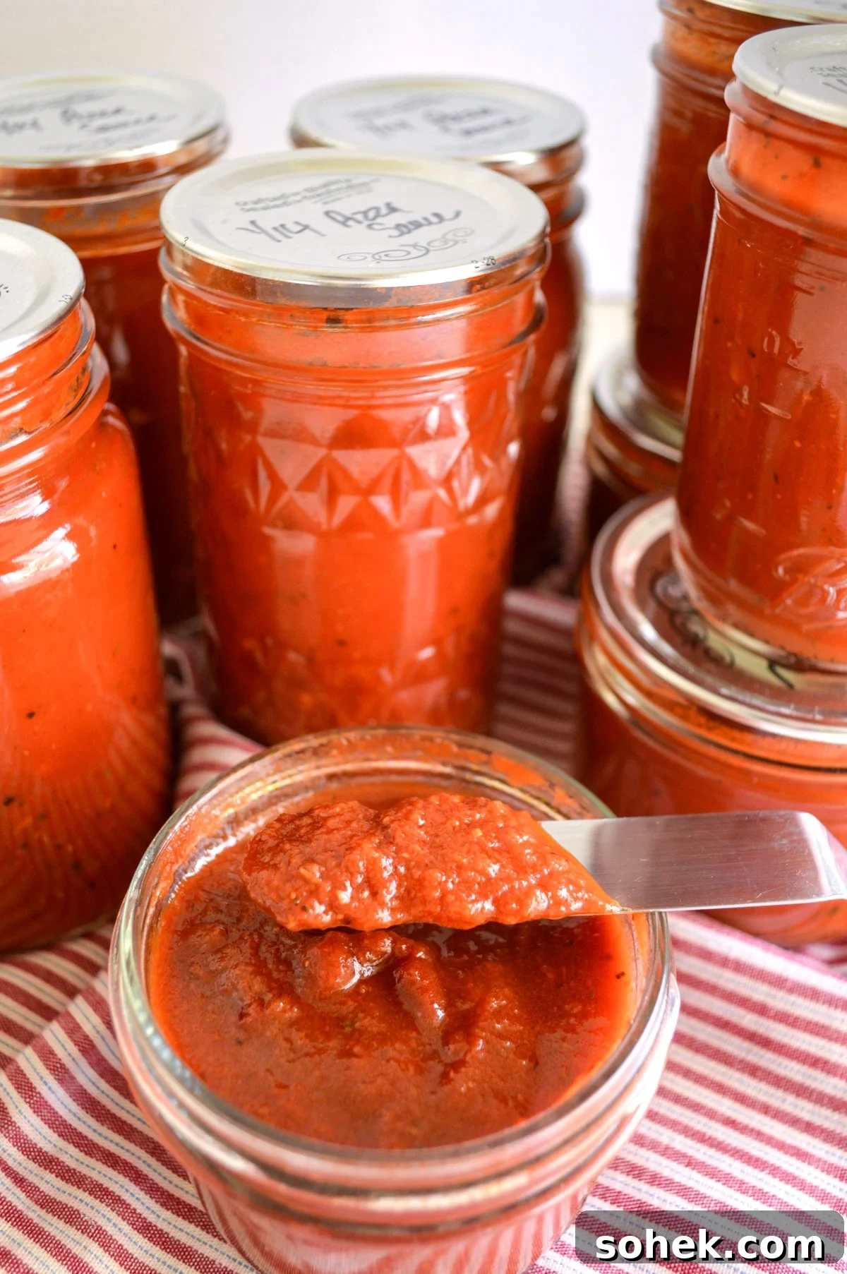 Canned Pizza Sauce from Fresh or Frozen Tomatoes — Simple Recipe 2 jars of pizza sauce with one open showing thickness on knife