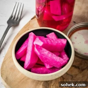 Pink pickled turnips in a bowl on a board.