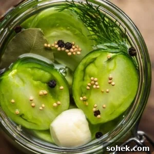 Overhead shot of a jar of pickled sliced green tomatoes and spices on a wooden board.