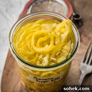 An open jar of pickled banana peppers on a wooden board.
