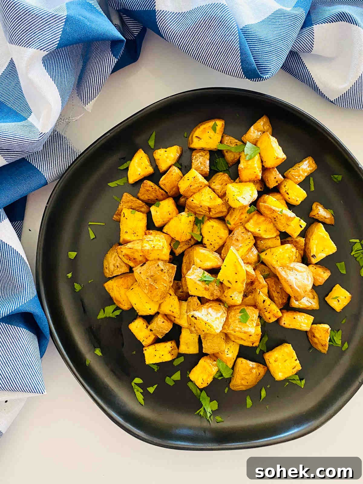 Crispy Air Fryer Diced Potatoes Recipe 2 diced potatoes cooked in air fryer on a plate with parsley garnish and a blue napkin
