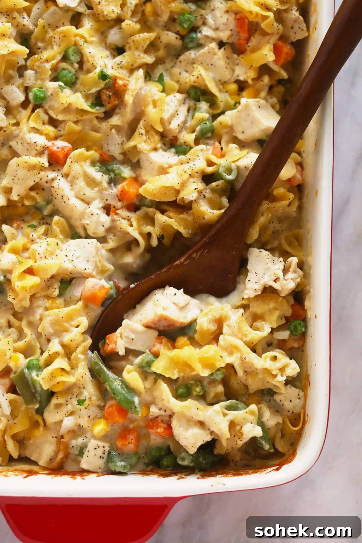 This Creamy Chicken Noodle Casserole is comfort food at its finest! Everything you love about chicken noodle soup, but as a flavor-packed casserole. Enjoy! Creamy chicken noodle casserole being scooped with a wooden spoon.