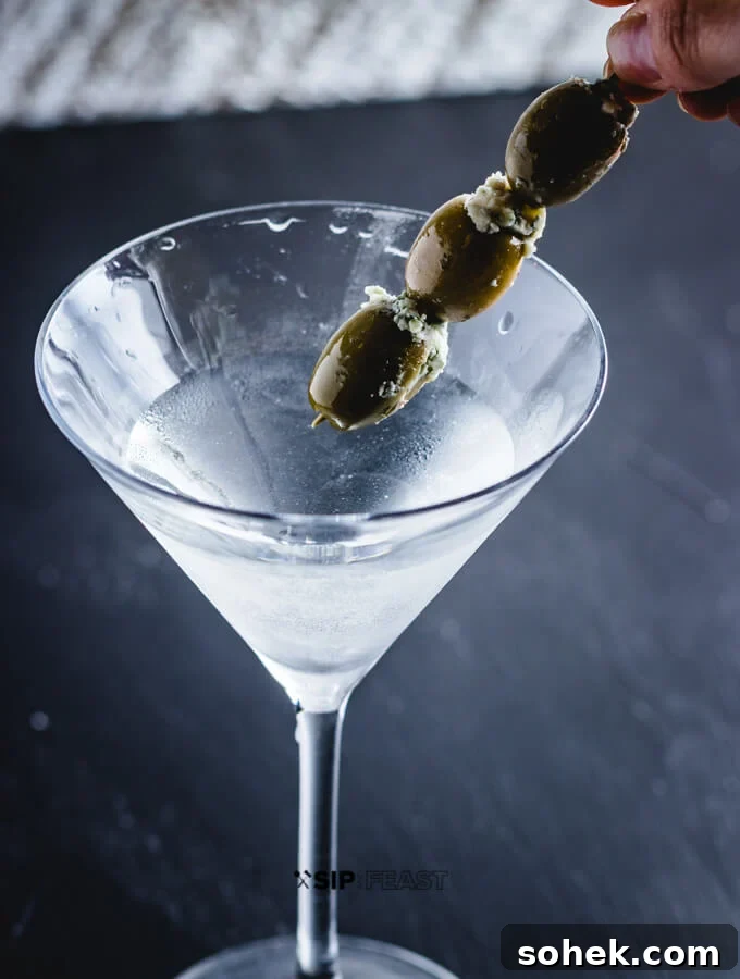 Placing 3 blue cheese olives into the martini.