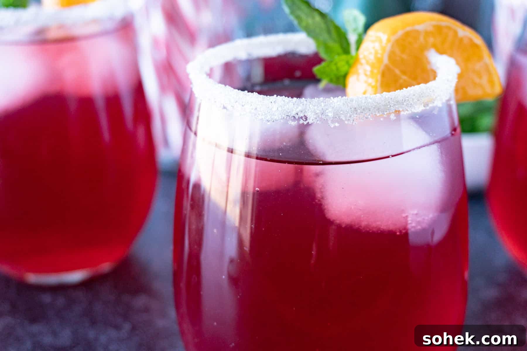 Cranberry Mint Julep Cocktail Recipe for Holiday Gatherings 9 Cranberry julep in glass with sugared rim and orange slice and mint leaves as garnish.
