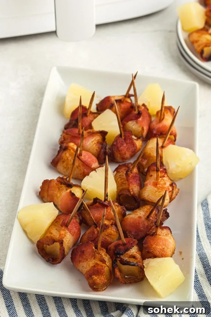 Crispy Air Fryer Bacon-Wrapped Pineapple Bites 2 Crispy bacon wrapped pineapple bites on a long white plate in front of the air fryer