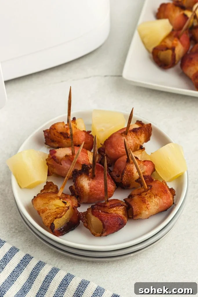 Crispy Air Fryer Bacon-Wrapped Pineapple Bites 7 Crispy bacon wrapped pineapple chunks on a small white plate