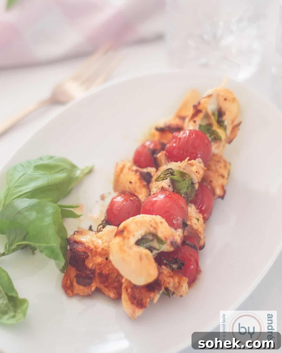 Mozzarella-Stuffed Grilled Chicken Skewers with Basil and Tomato 3 A top-down photo of a platter of three chicken skewers filled with mozzarella and basil with tomatoes.