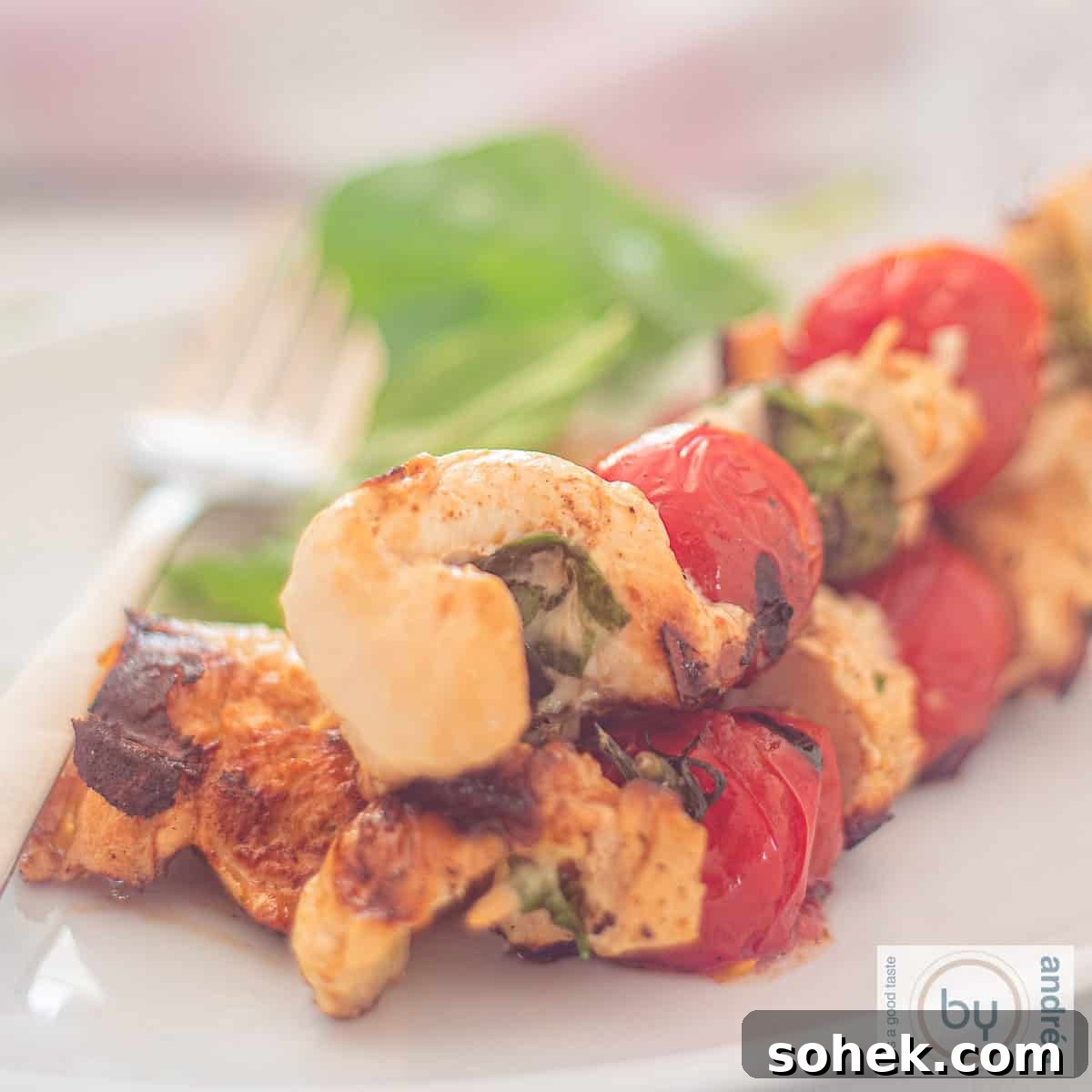 Mozzarella-Stuffed Grilled Chicken Skewers with Basil and Tomato 4 A square photo of three skewers with chicken, basil, mozzarella and tomatoes.