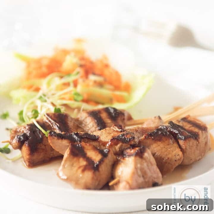 A square photo of a white plate with three skewers of pork tenderloin with ketjap and a salad with carrot and cucumber in the background