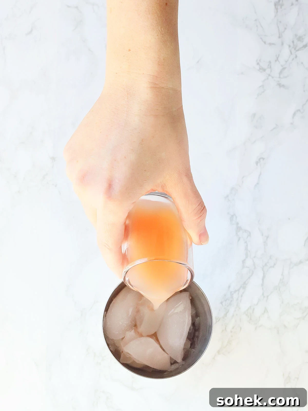 Rosemary Gin Grapefruit Cocktail Recipe with Citrus Twist 6 hand pouring a shot glass of grapefruit juice into a metal shaker full of ice