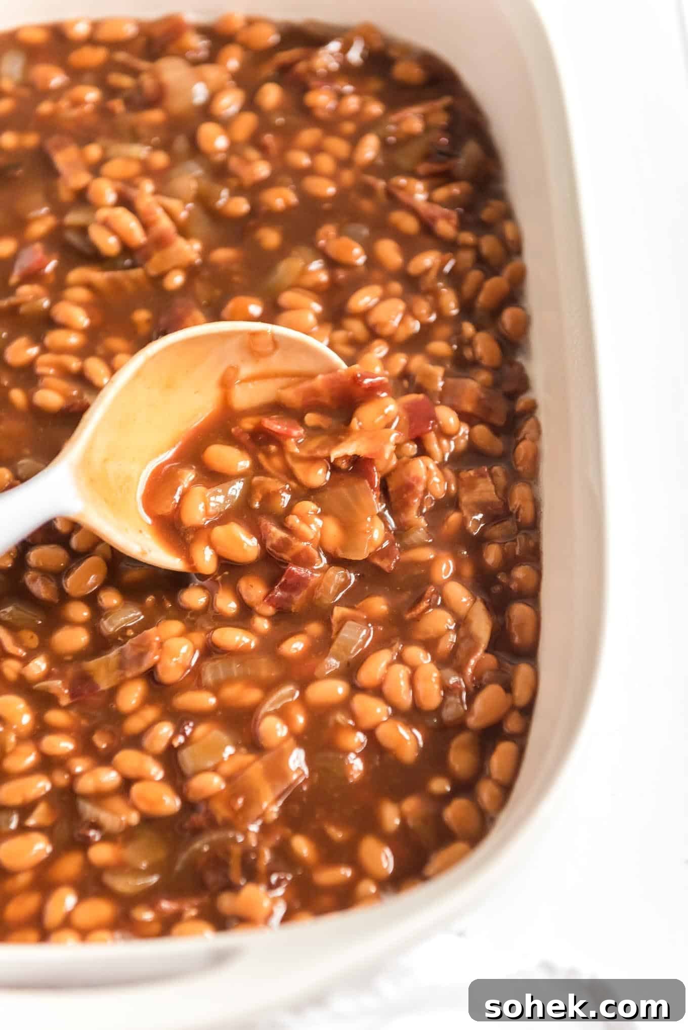 A spoon scooping some of the beans with bacon from the dish.