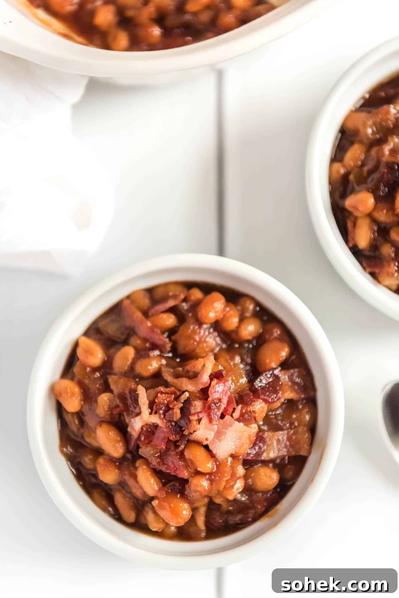 Small ramekin of baked beans with bacon on the counter.