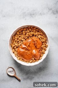 Chocolate Peanut Butter Muddy Buddies Recipe 4 A large mixing bowl of Chex cereal, with a melted peanut butter chocolate mixture poured on top.