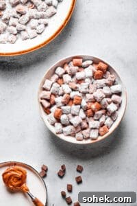 Chocolate Peanut Butter Muddy Buddies Recipe 7 Muddy buddies in a white bowl, with a spoonful of peanut butter and a larger serving dish of the snack nearby.