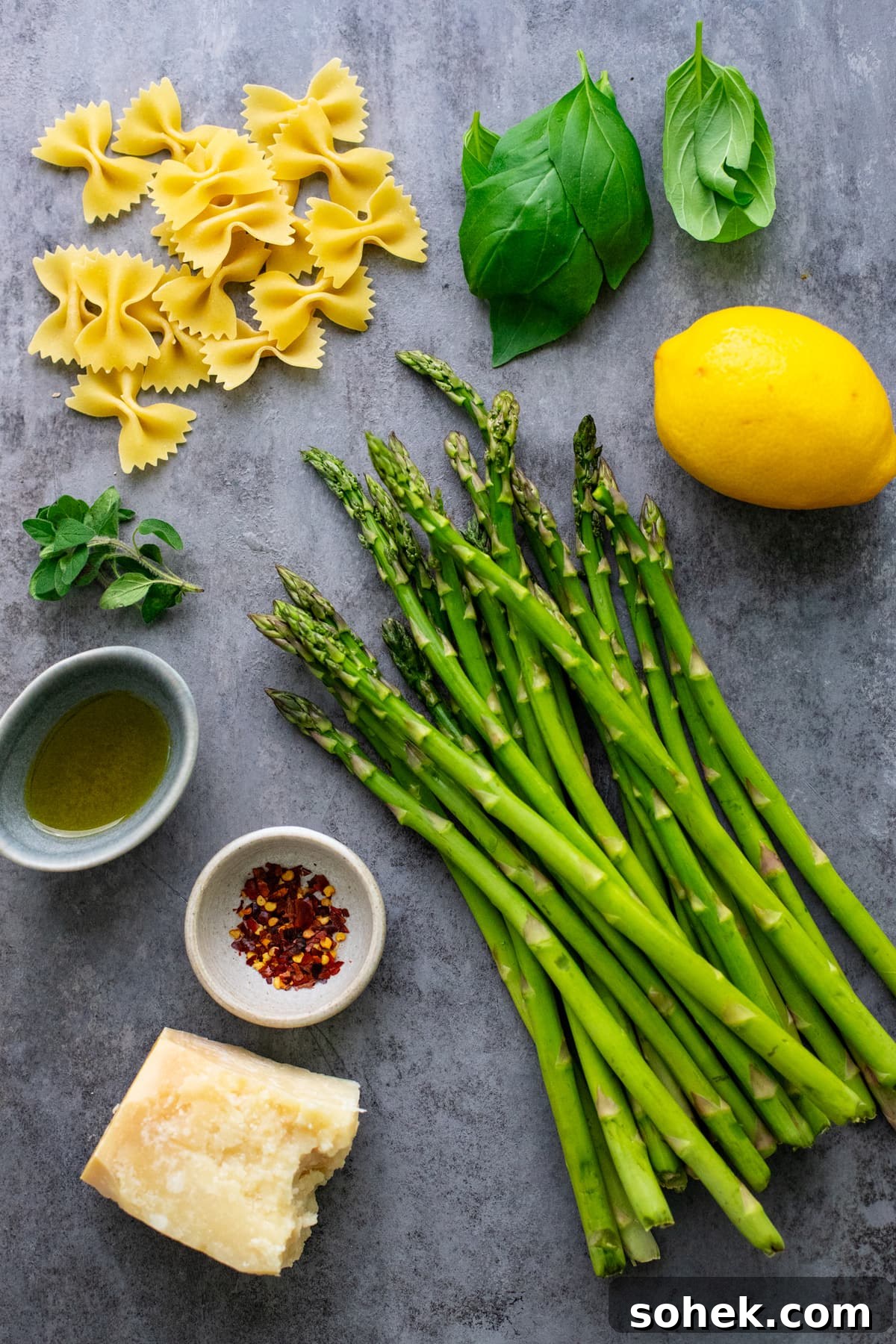 ingredients for asparagus pasta arranged on a dark gray background.