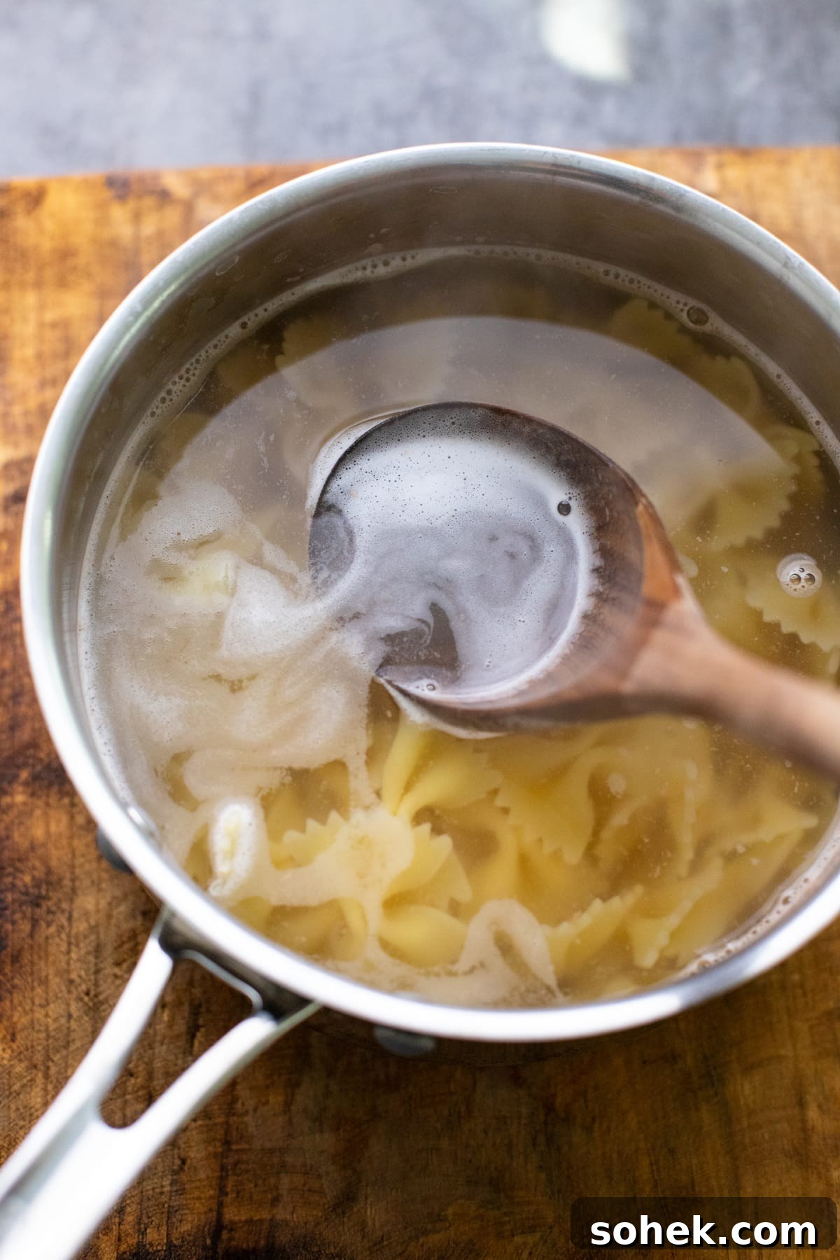 wooden ladle scooping up water in a pot with pasta noodles in it.
