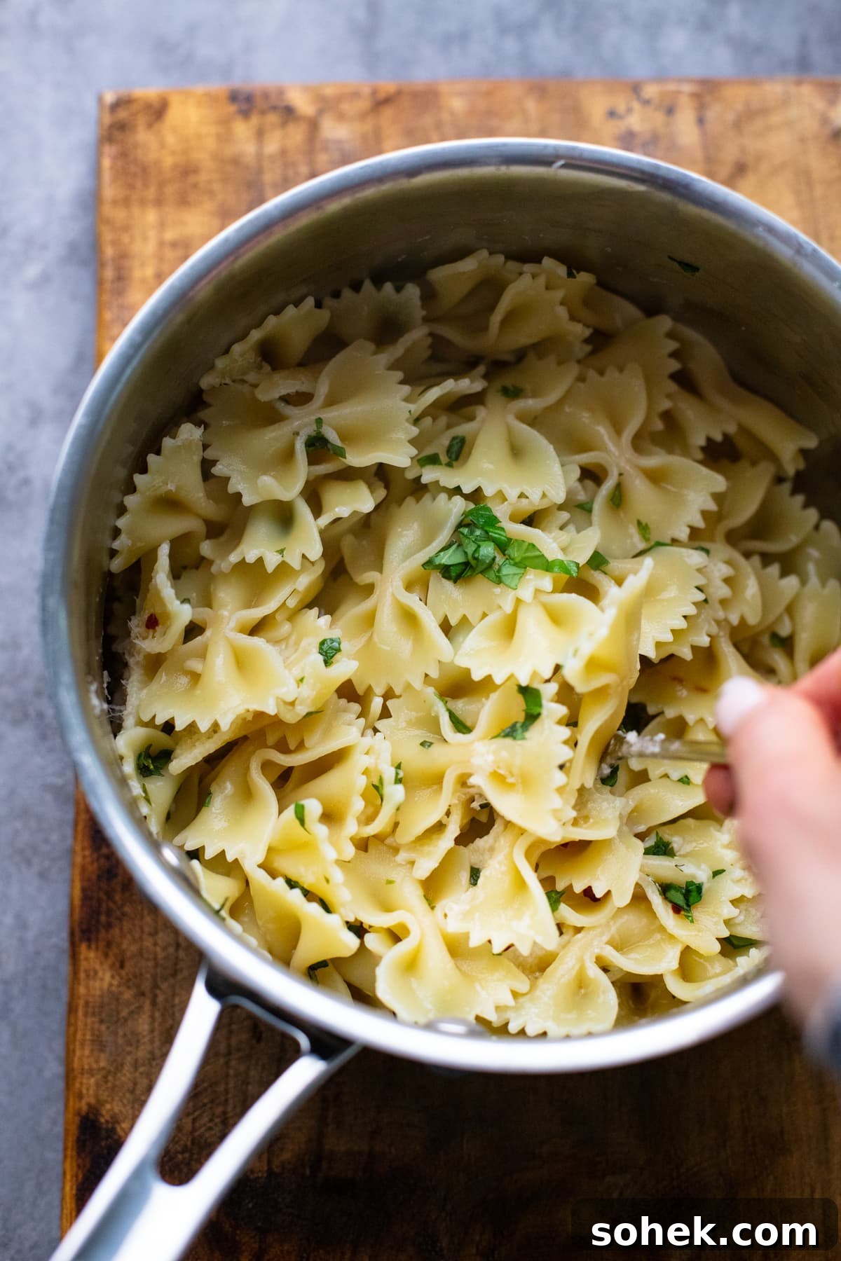 hand using spoon to stir bowtie pasta in pot.