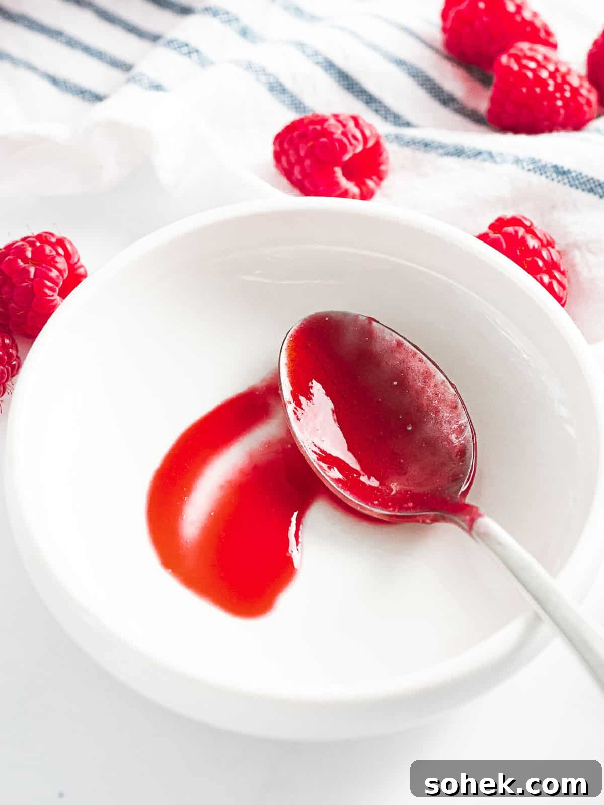 Homemade Raspberry Sauce Recipe for Desserts and Toppings 8 Raspberry sauce drizzled on a plate with a spoon running through it to show the thickness.