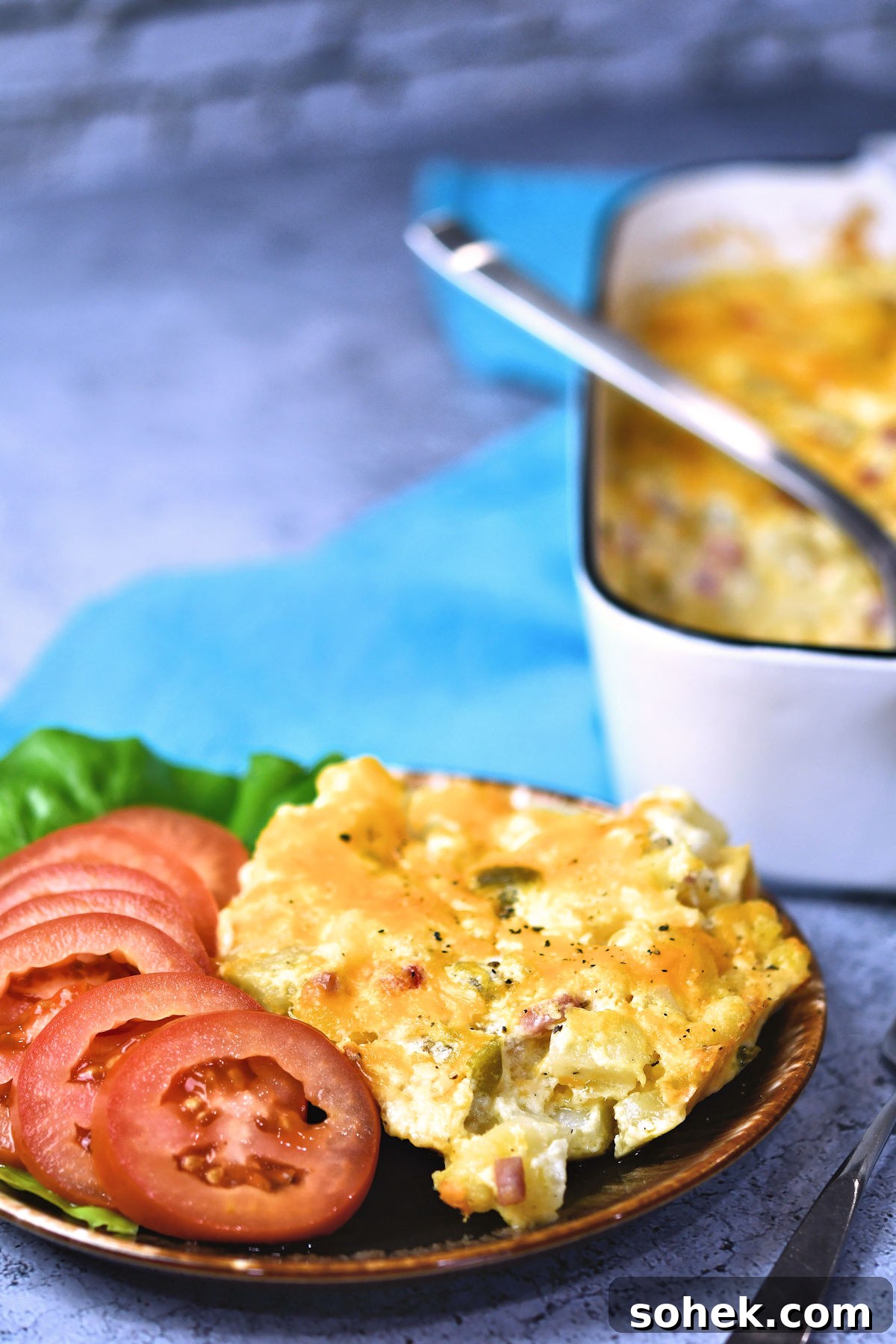 A serving of potato breakfast casserole, on a plate, served with sliced tomatoes.