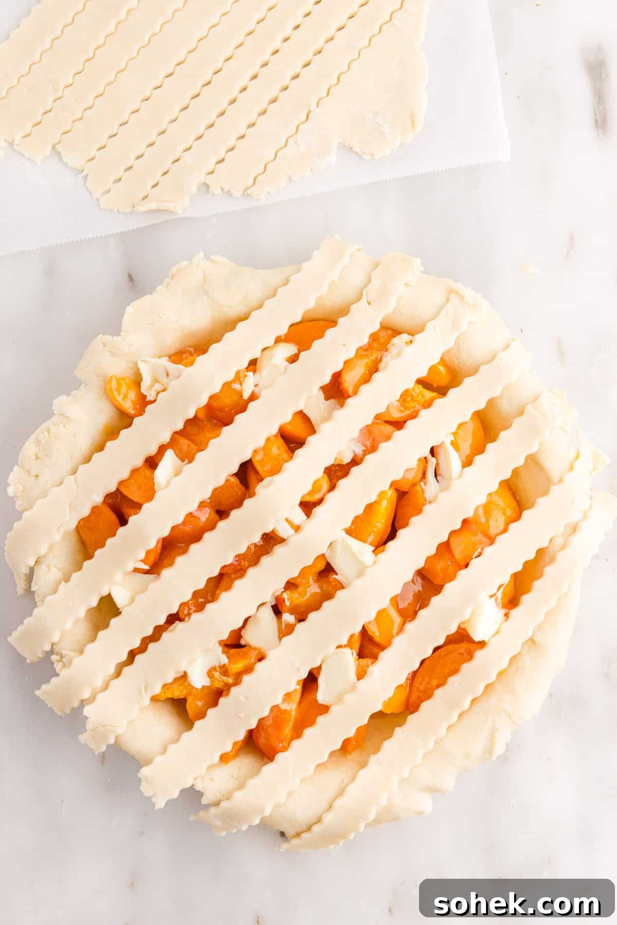 Strips of pie crust lying parralel over apricot pie filling.