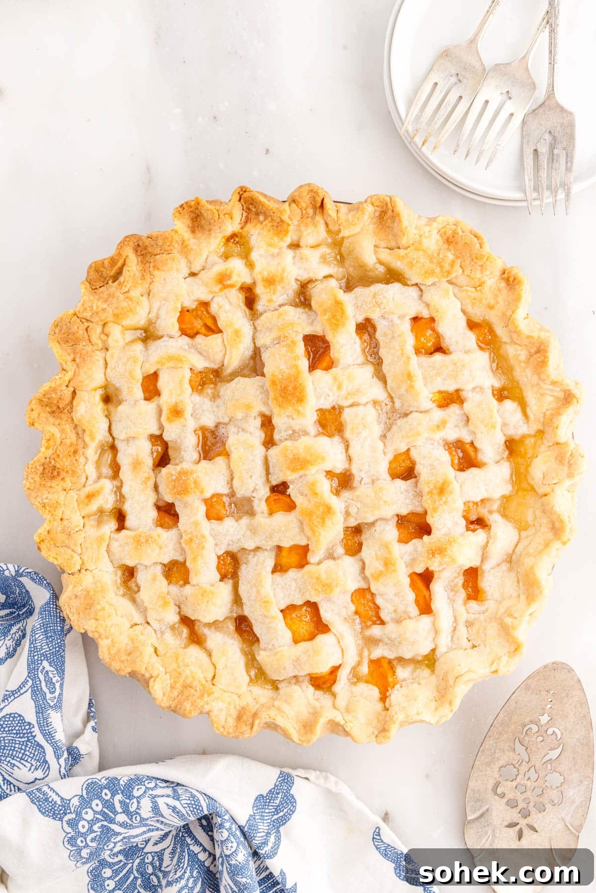 Baked apricot pie with pie server, dishes and forks, and floral linen.