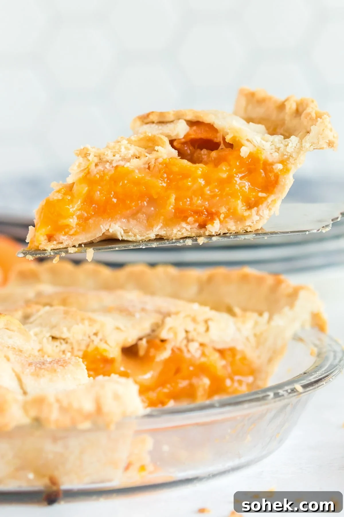 Slice of apricot pie lifted on a pie server over the pie dish.
