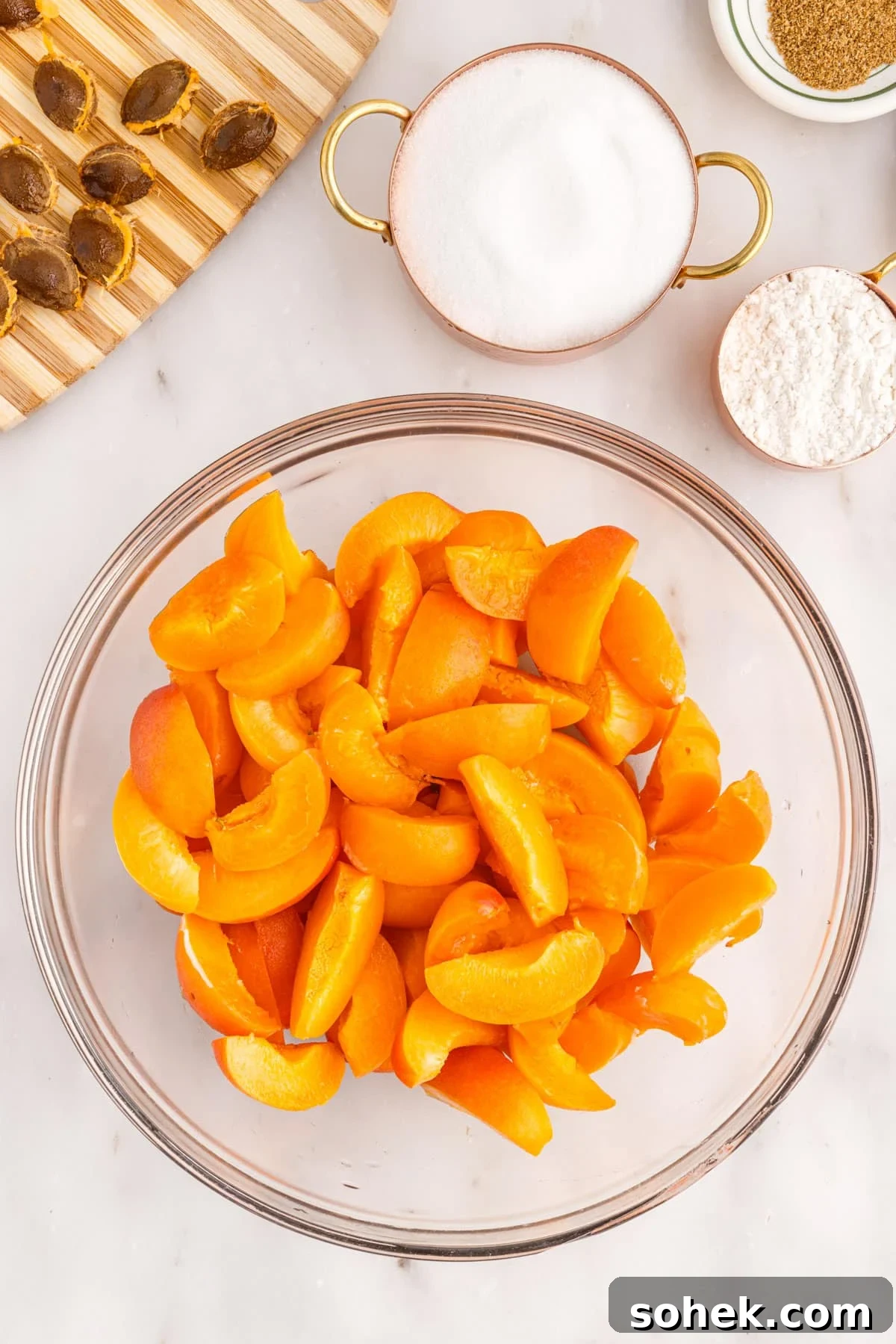 Sliced apricots in glass bowl with dishes of sugar and flour beside.