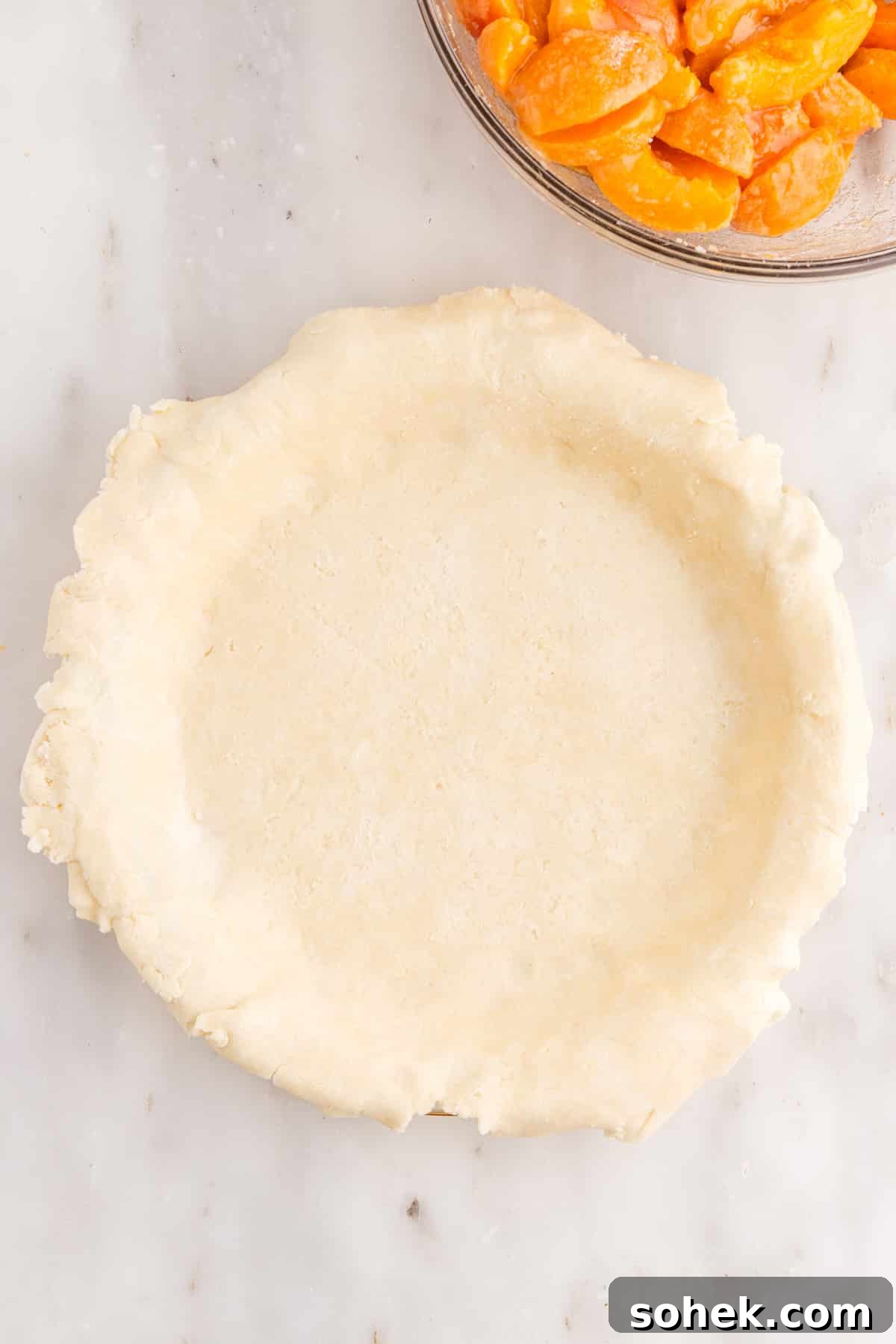 Pie crust bottom set in pie plate, bowl of apricot pie filling.