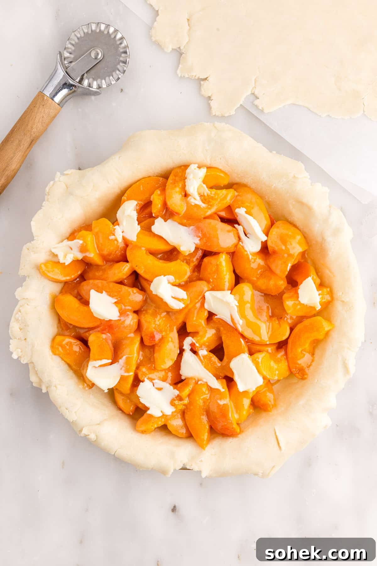 Dots of butter over apricot pie filling in pie plate.