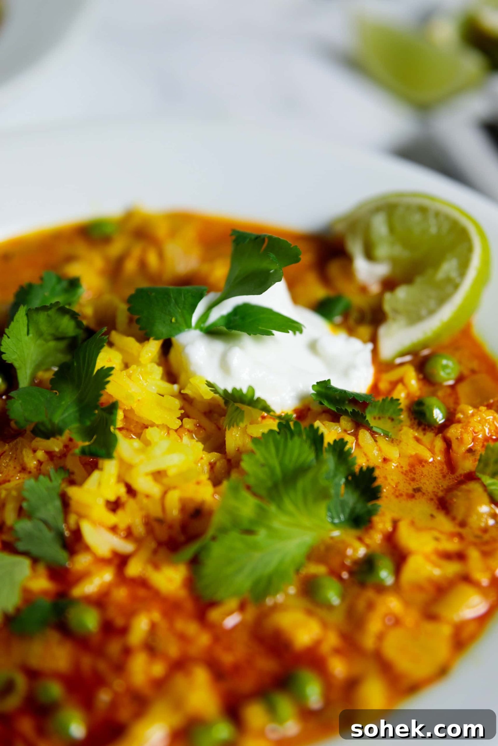 Slow Cooker Cauliflower Curry Soup Recipe 3 Close up view of orange colored cauliflower curry soup sitting on marble surface topped with cilantro pieces and slice of lime with dollop of sour cream