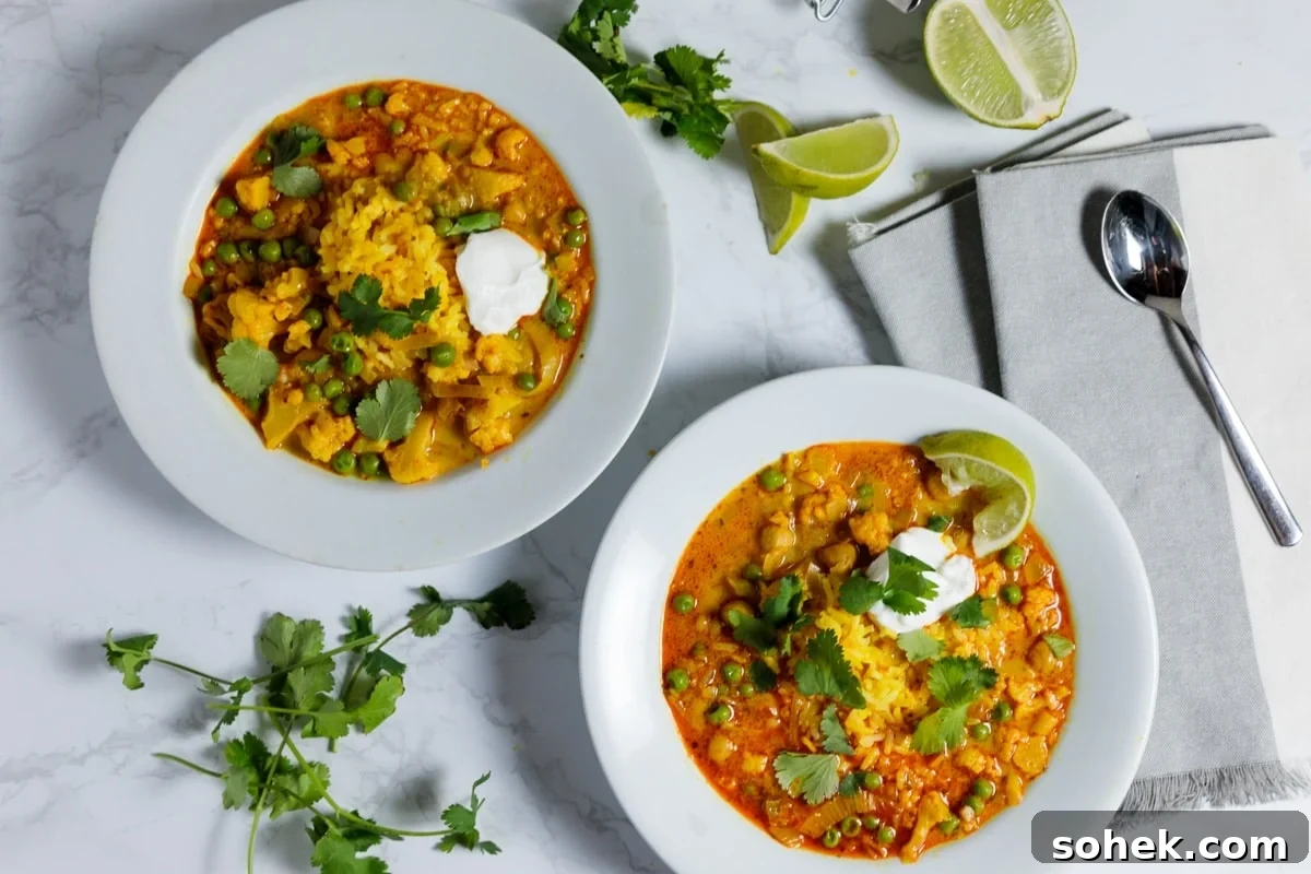 Slow Cooker Cauliflower Curry Soup Recipe 4 Two bowls filled with orange colored slow cooker cauliflower curry soup sitting on marble surface topped with cilantro and lime slices