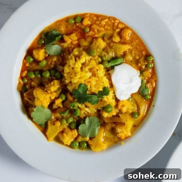 Slow Cooker Cauliflower Curry Soup Recipe 5 White bowl filled with slow cooker cauliflower curry soup with dollop of yogurt and sprinkling of parsley on top.
