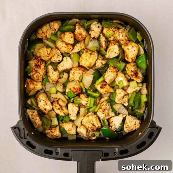A bird's eye view of an air fryer filled with cajun chicken, green peppers, onion and celery.