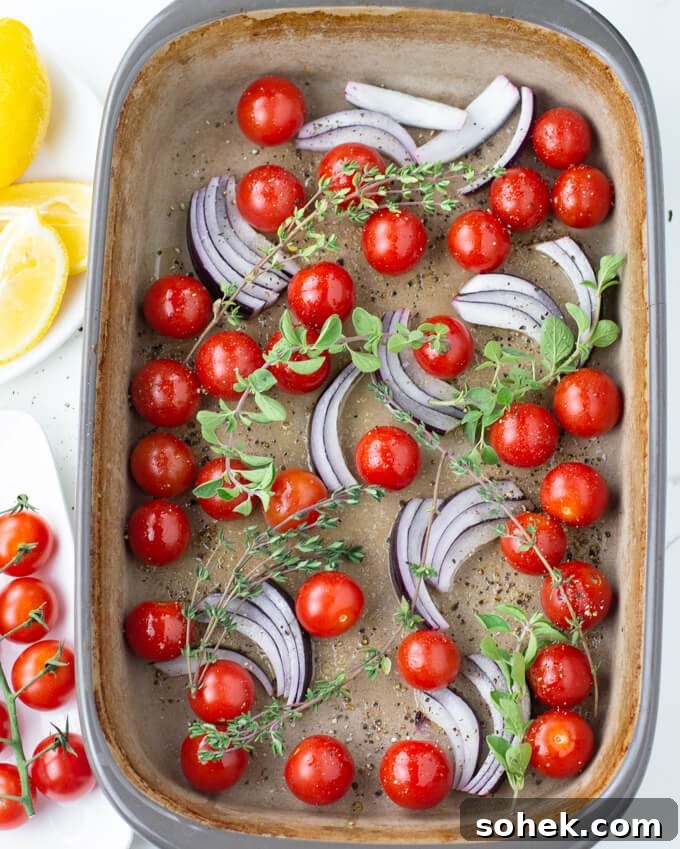 Oven-Baked Cod with Roasted Blistered Tomatoes 4 Cherry tomatoes, sliced red onion and sprigs of oregano and thyme all are in a baking dish. Cherry and lemon wedges sit next to the dish.