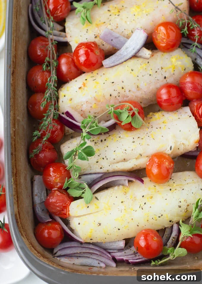 Oven-Baked Cod with Roasted Blistered Tomatoes 5 Four pieces of cod fillets sit in a baking dish with cherry tomatoes, red onions slices and sprigs of oregano and thyme are scattered around the cod.