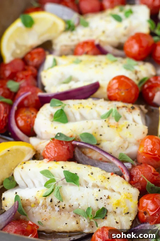 Oven-Baked Cod with Roasted Blistered Tomatoes 7 Baked Cod with cherry tomatoes, red onions and lemon wedges are in a baking dish with fresh oregano scattered on top. A bowl of black rice sits next to it.