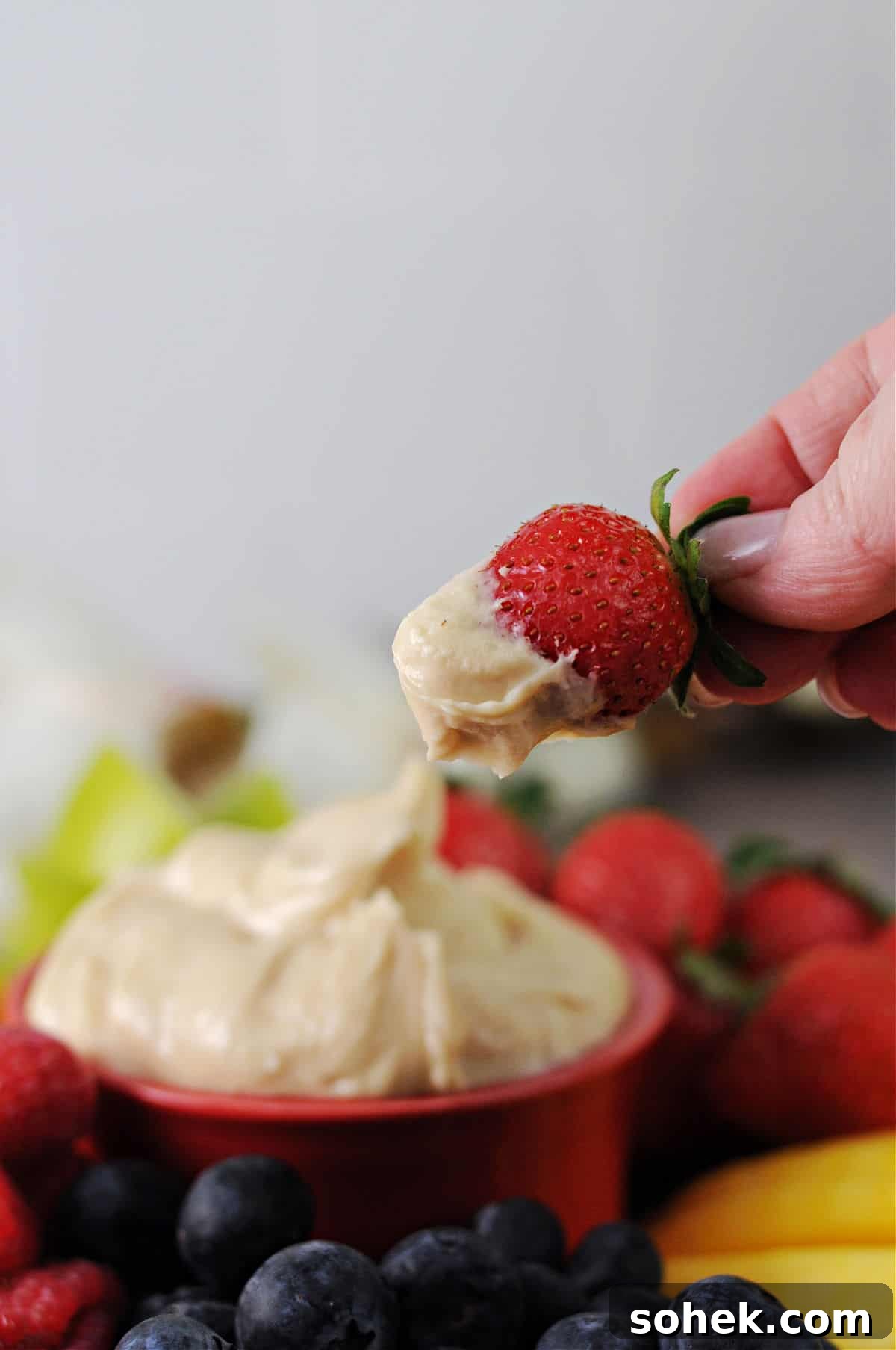 Cream Cheese Fruit Dip: 3-Ingredient Recipe for Parties 6 hand holding a strawberry that's been dipped in the cream cheese and brown sugar fruit dip.