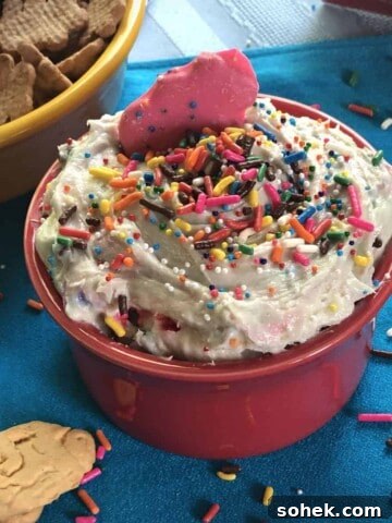 Dunkaroo Dip, also known as funfetti cake batter dip, in a small bowl garnished with sprinkles and surrounded by crackers and cookies for dipping