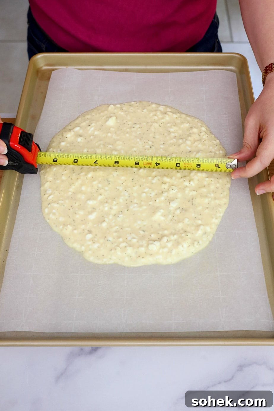 Cottage Cheese Pizza Crust Recipe: Thin, Chewy Low-Carb Base 6 Batter spread into a circle on parchment paper with a tape measure showing the diameter of 10 inches.