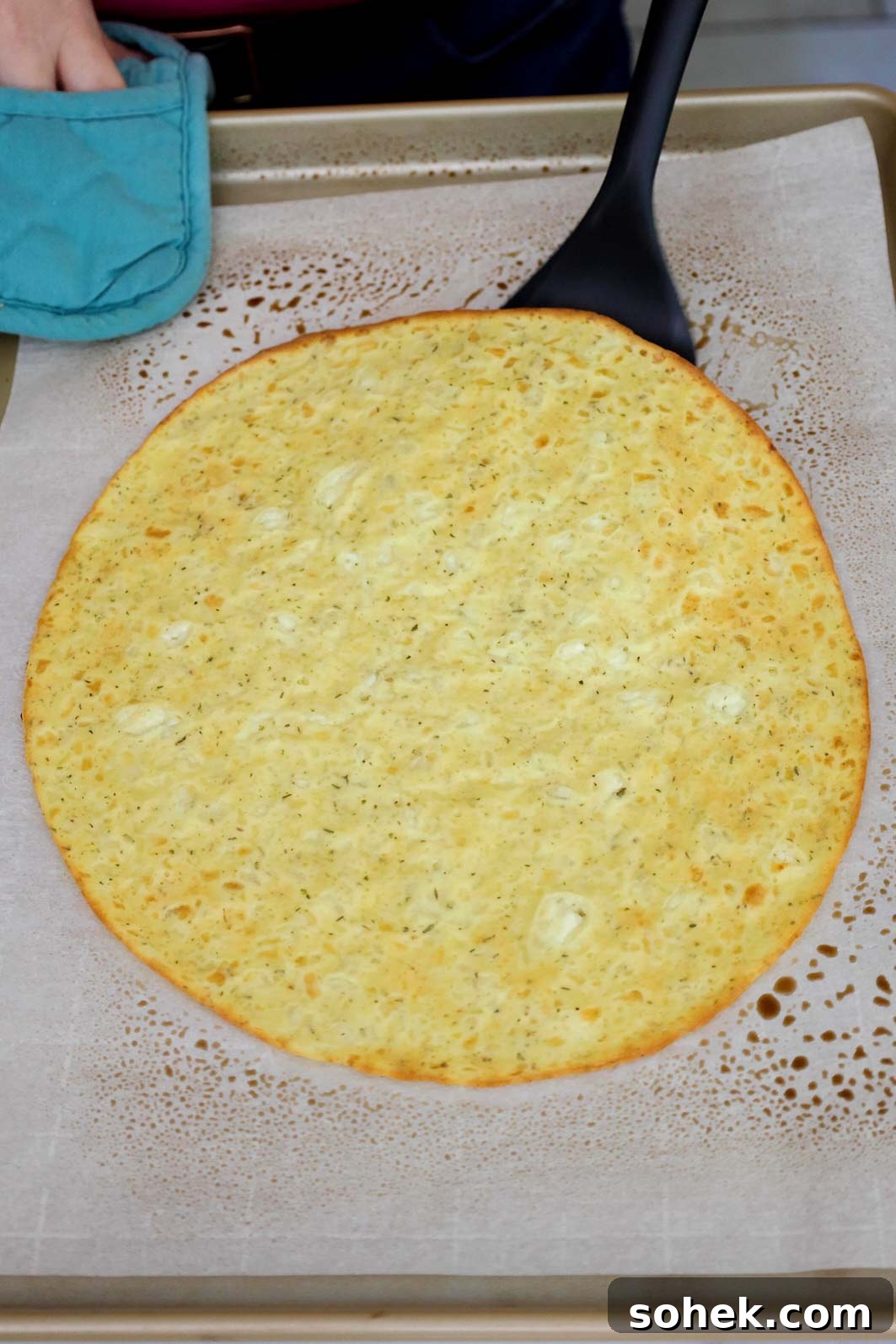 Cottage Cheese Pizza Crust Recipe: Thin, Chewy Low-Carb Base 7 A baked pizza crust on a parchment-lined baking sheet being flipped with a spatula.