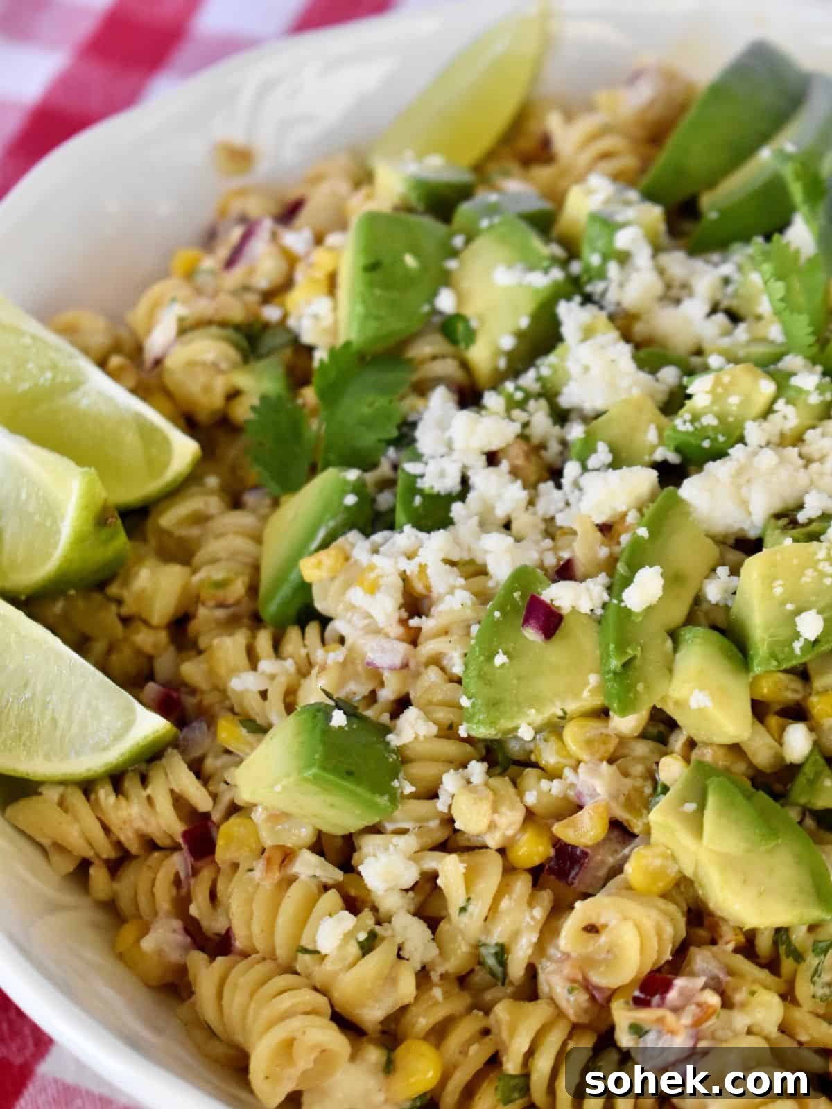 Mexican Elote Pasta Salad: Creamy Street Corn Pasta Recipe 2 Elote Pasta Salad in a white bowl with lime wedges and avocado on top.