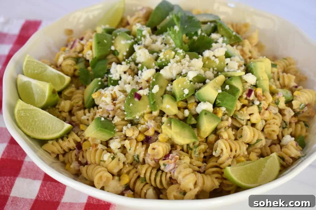 Mexican Elote Pasta Salad: Creamy Street Corn Pasta Recipe 7 Elote Pasta Salad with avocado and cotija cheese and lime wedges on the side.
