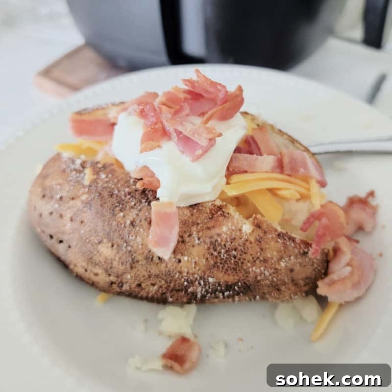 Air fryer baked potato topped with sour cream, bacon, and cheddar cheese
