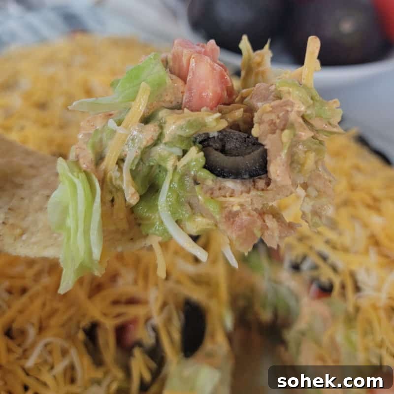 Tortilla holding 7 layer taco dip above a full casserole dish
