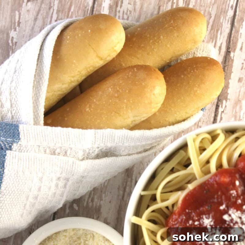 Olive Garden breadsticks wrapped in a cloth next to a bowl of spaghetti