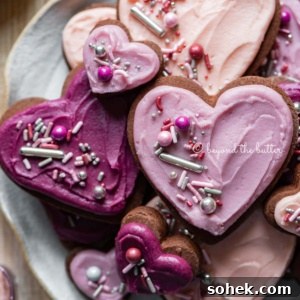 Chocolate Cut-Out Cookies: Decadent Cocoa Sugar Cookies for Decorating 11 Plate full of heart-shaped chocolate cut out sugar cookies decorated with buttercream frosting and sprinkles.