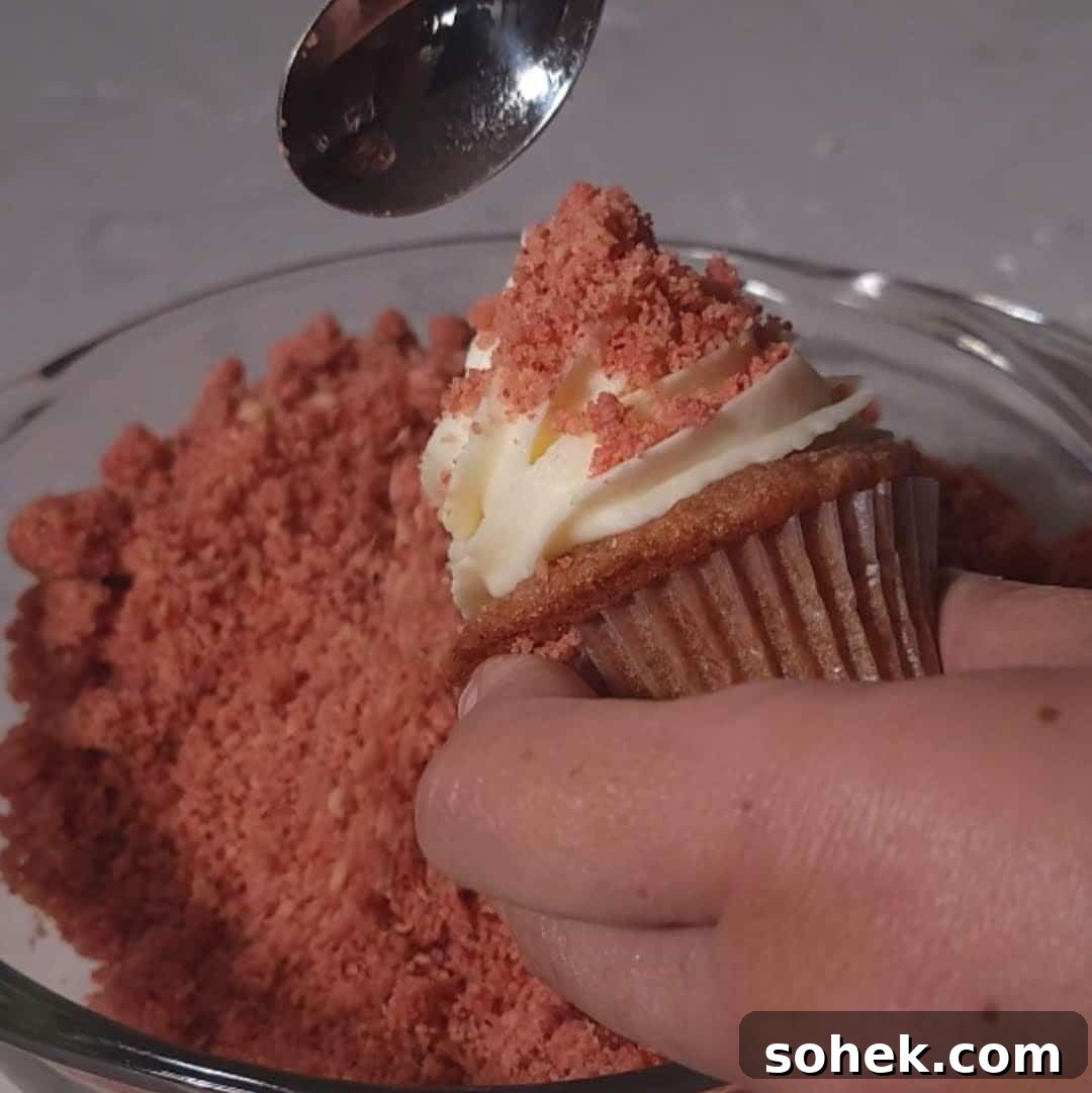 Strawberry Crunch Cupcakes Recipe with Crispy Topping 12 Decorating a strawberry crunch cupcake by dipping the frosted top into bright red crumbs for added texture.